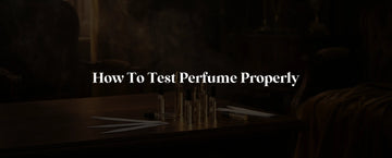 Luxury perfume sample vials and testing blotter strips on a dark wooden surface with warm amber lighting and atmospheric smoke